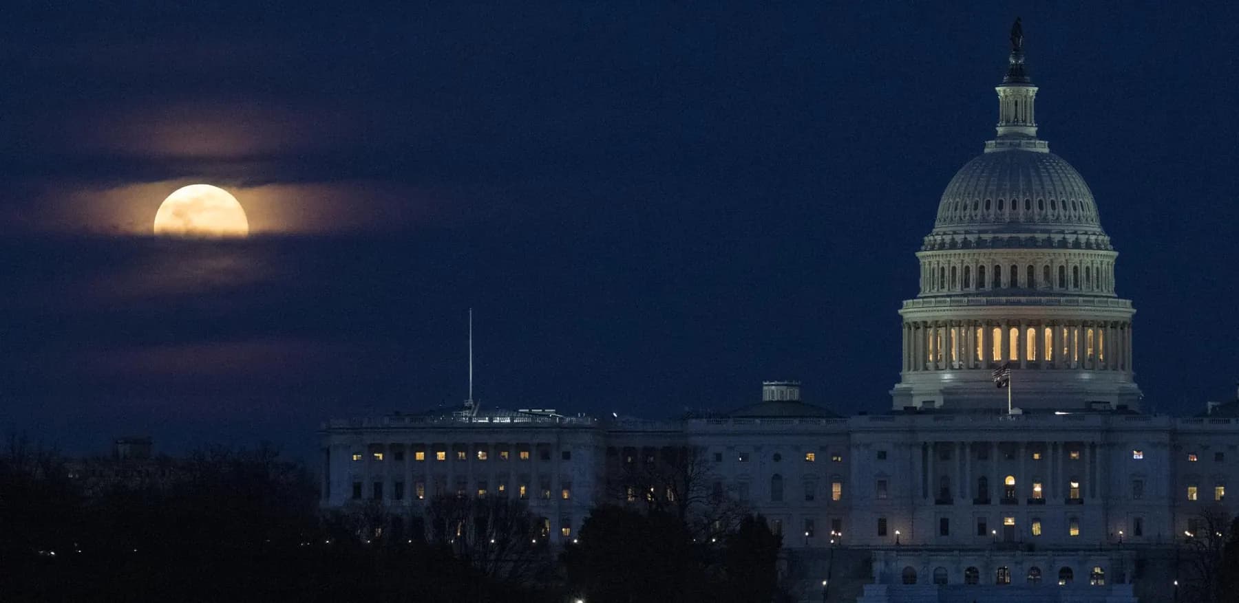 A full Moon rising behind the dome of the United States Capitol at dusk