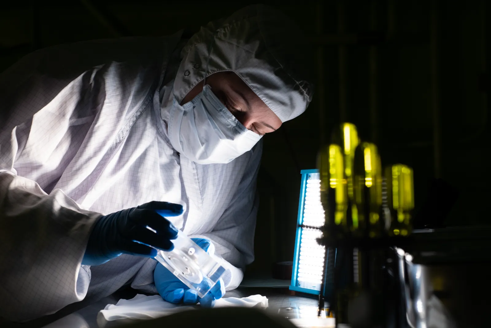 A technician in cleanroom dress inspecting an optical component