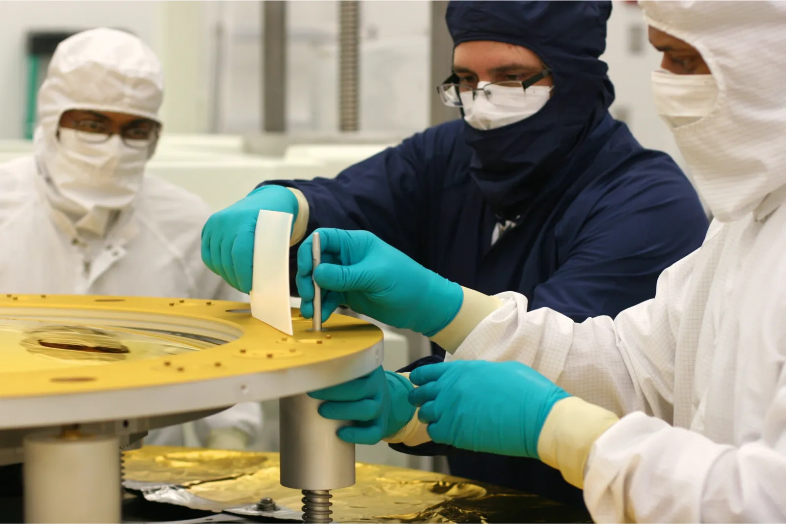 Technicians in cleanroom dress fitting hardware to a mirror mount