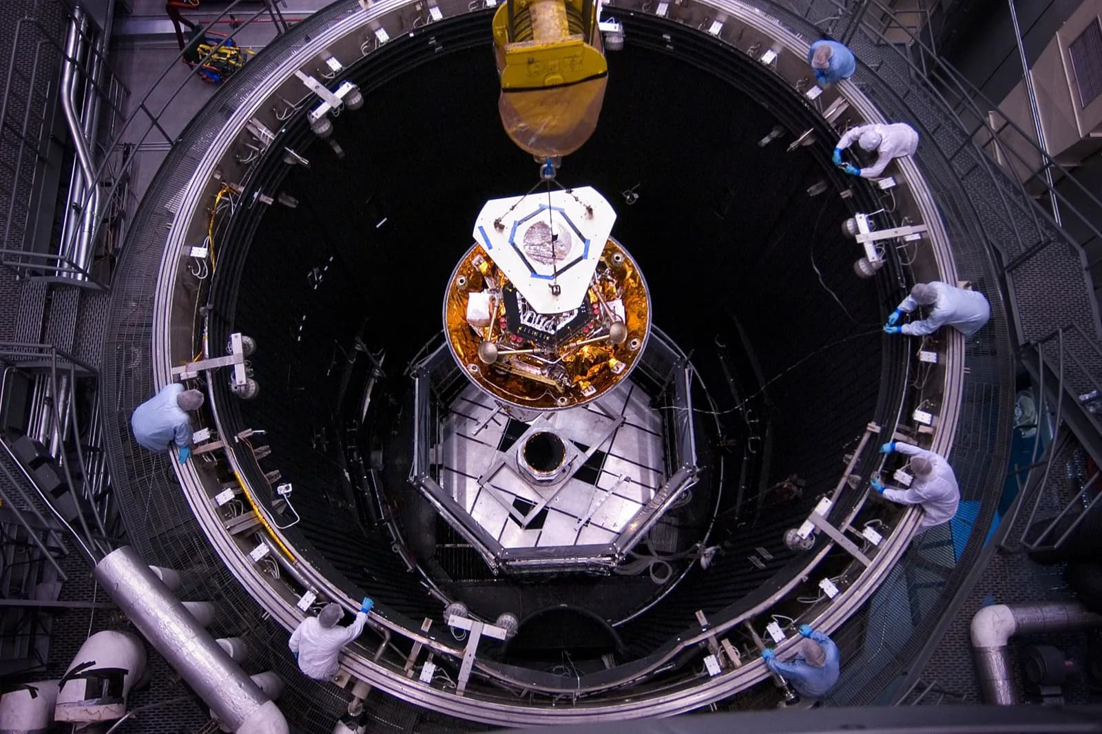 Looking down into a thermal vacuum chamber as hardware is lowered in