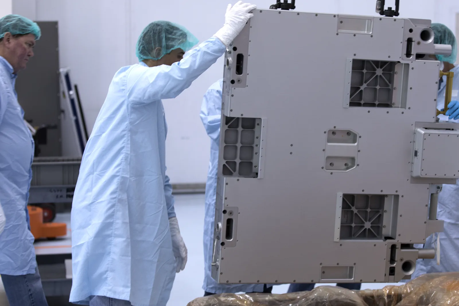 Technicians guiding flight hardware on a crane hook