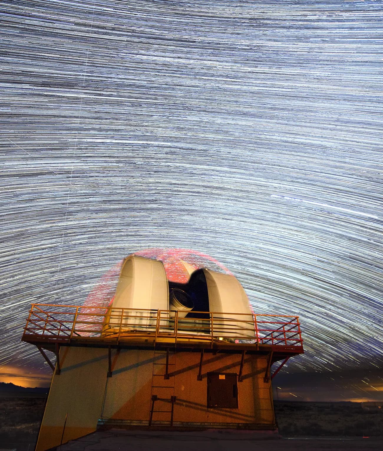 Star trails wheeling over the open dome of a space surveillance telescope at night