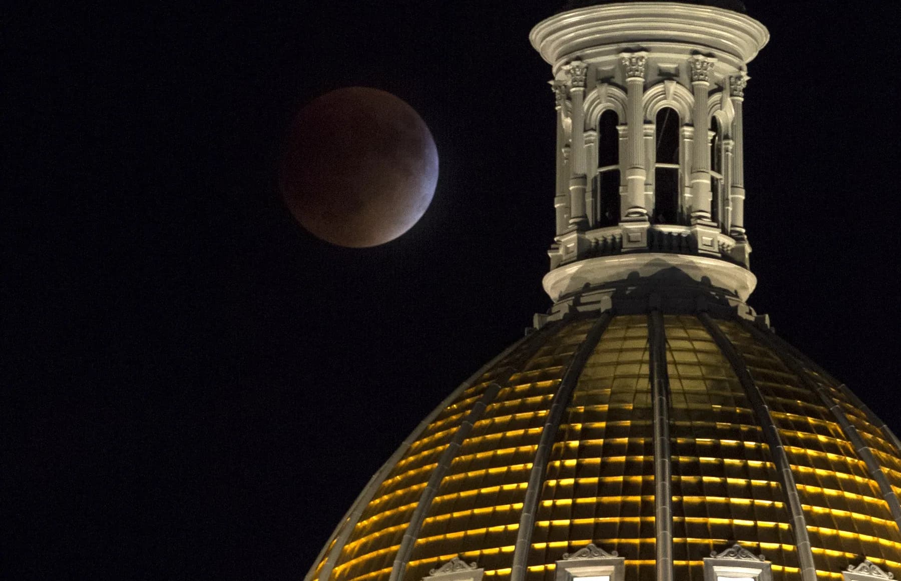 A total lunar eclipse beside the gold dome of the Colorado State Capitol in Denver at night